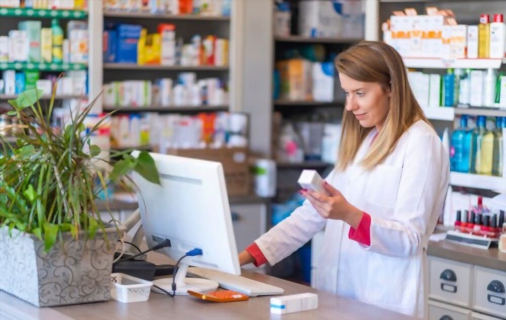 Farmacéutica en el mostrador de la farmacia utilizando ordenador para gestión y dispensación de medicamentos.